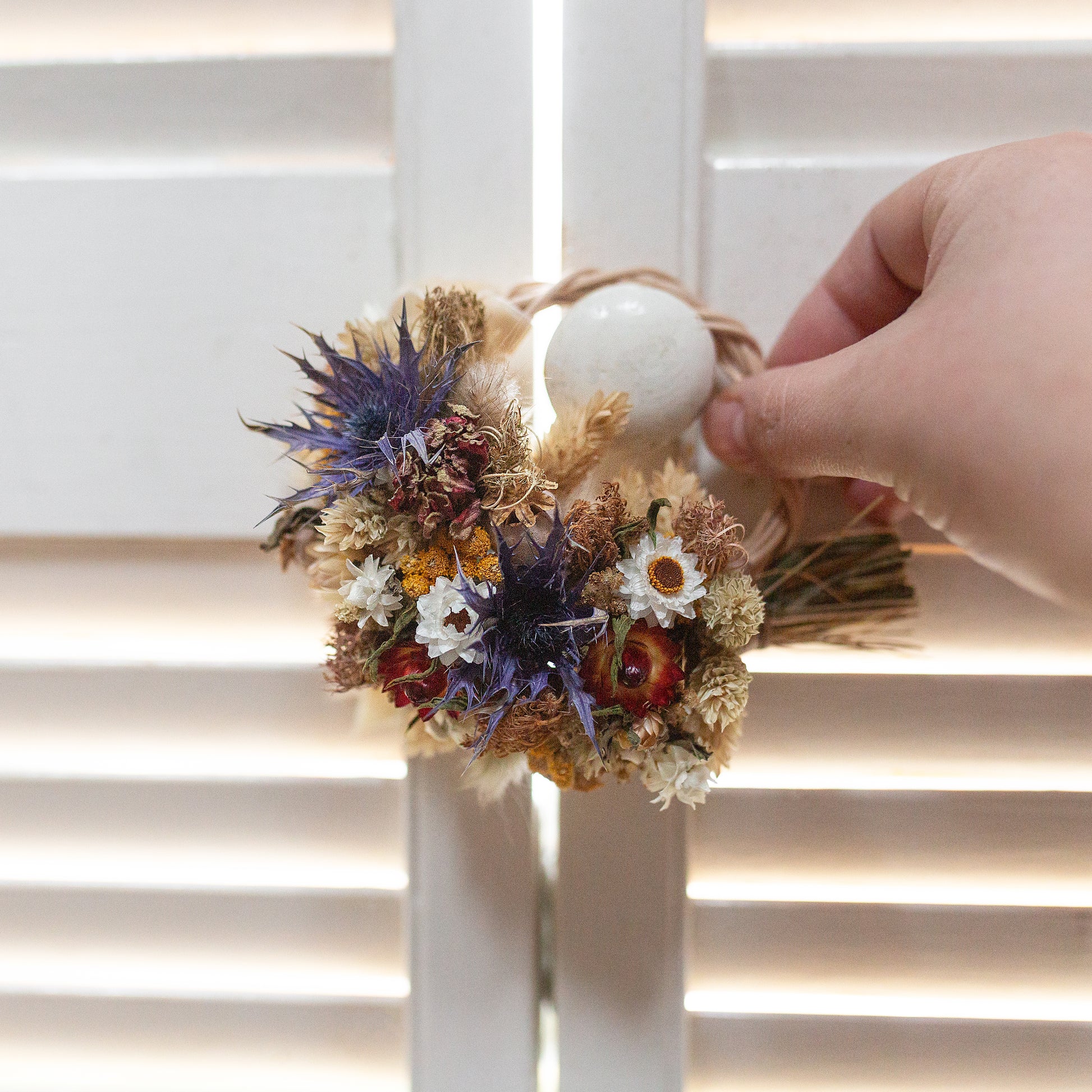 small mini blue yellow and red hand sized wreath being hung on a white shutter handle 