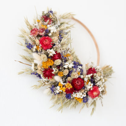 wood wreath hoop close up. the wreath is half covered in dried flowers. red, white blue and yellow.