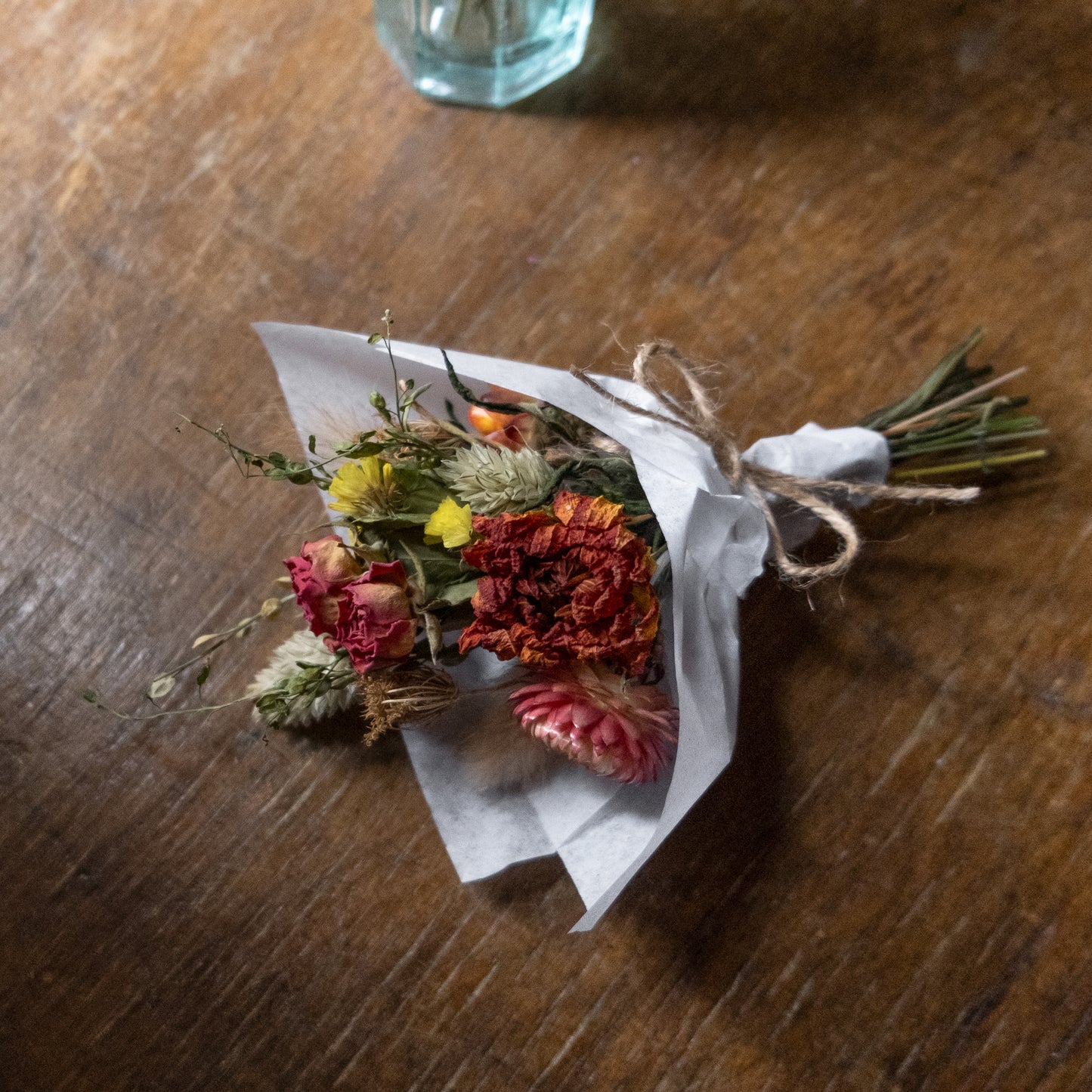 Small bouquet posy made of dried flowers wrapped in white tissue paper laid on a wooden table