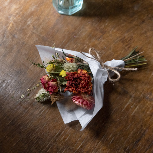 Small bouquet posy made of dried flowers wrapped in white tissue paper laid on a wooden table