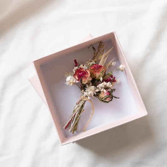 posy made from dried flowers tied together with twine in a gift box. the box inside is white and the outside is pink. The box is on a light background