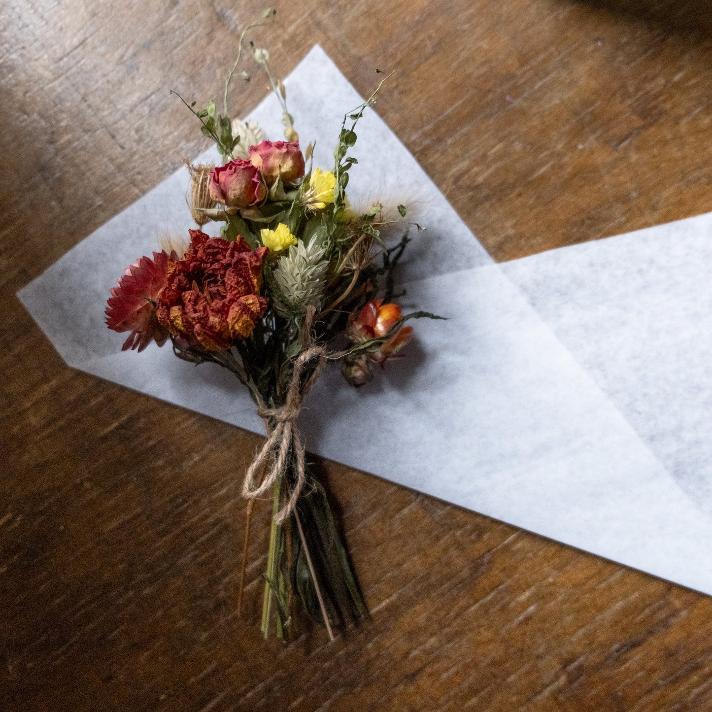 orange autumn feel dried flower posy tied with twine laid on white tissue ready to be wrapped on a wooden surface