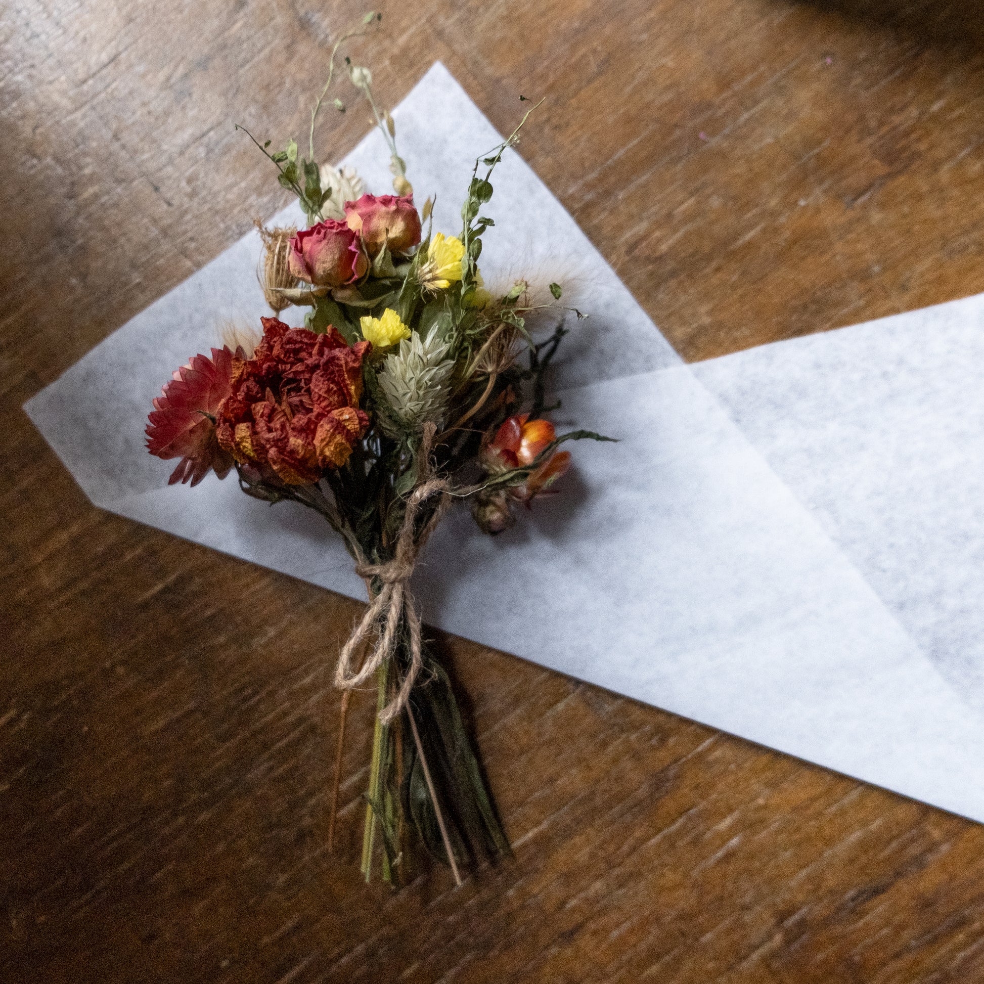 orange autumn feel dried flower posy tied with twine laid on white tissue ready to be wrapped on a wooden surface