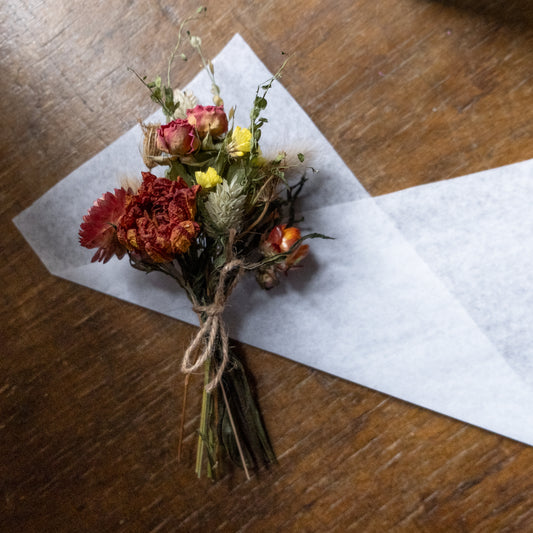 orange autumn feel dried flower posy tied with twine laid on white tissue ready to be wrapped on a wooden surface