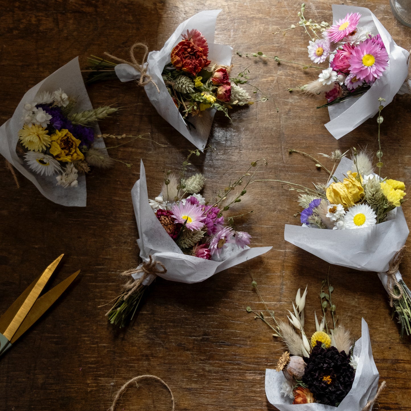 Small flower posies laid on a wooden table. The posies are different colours an d are tied together with natural twine and wrapped in white tissue paper