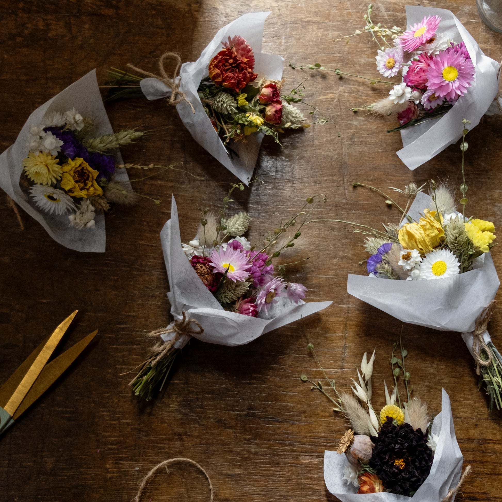Small flower posies laid on a wooden table. The posies are different colours an d are tied together with natural twine and wrapped in white tissue paper