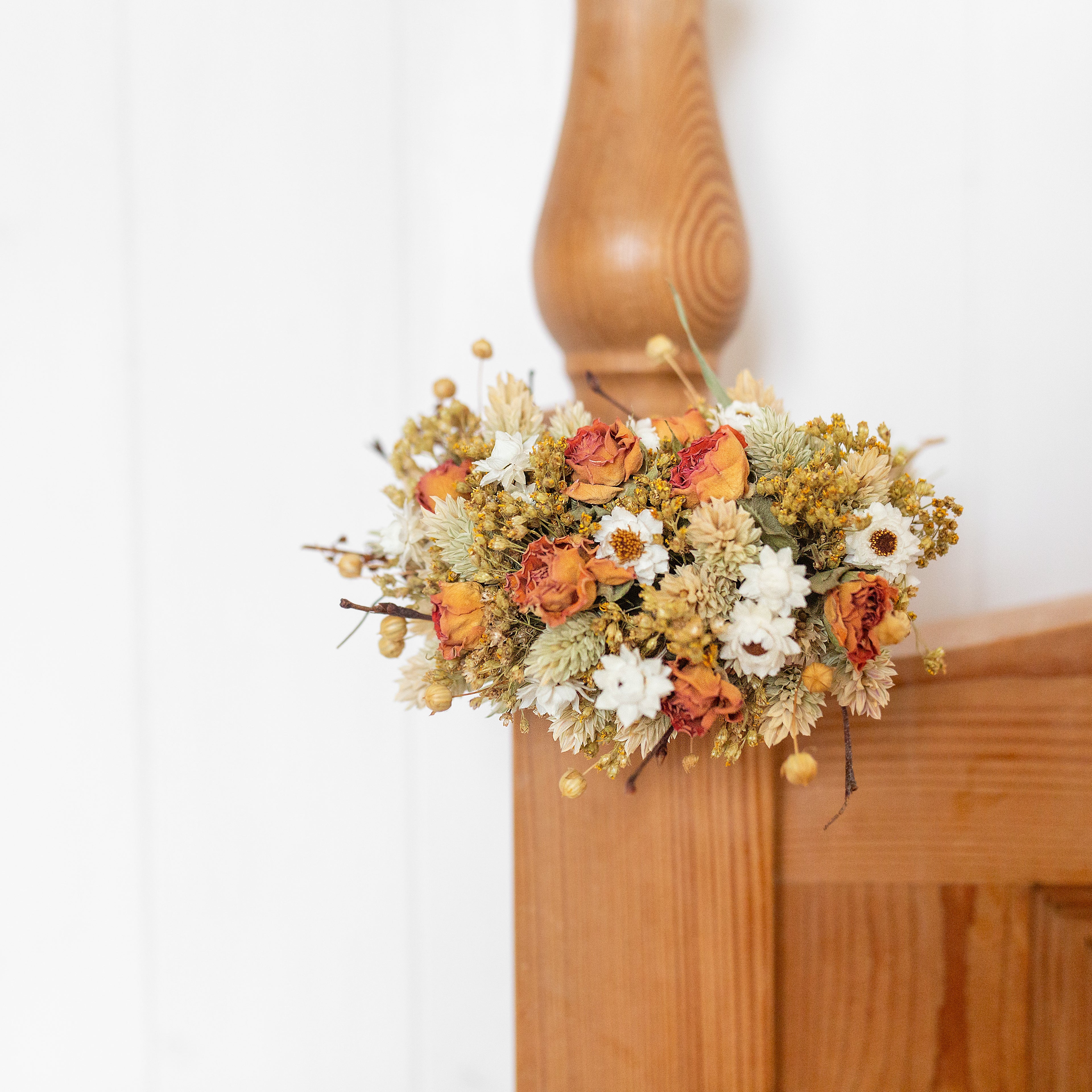 small orange white natural dried flower wreath hung on a bed post