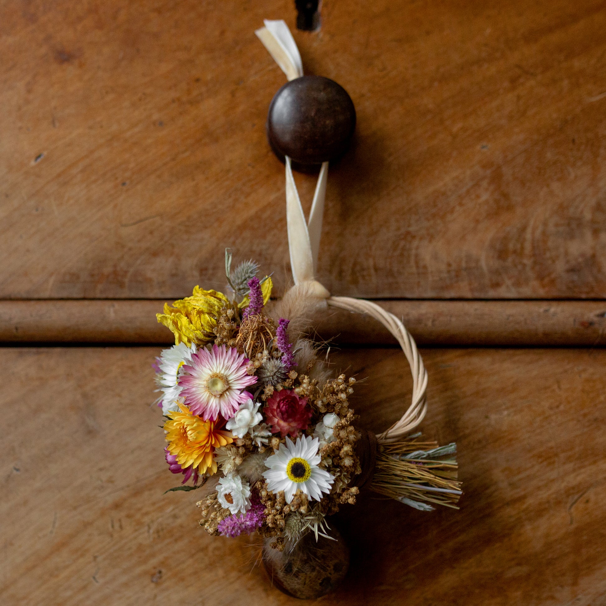 dried flower mini wreath hanging hung on via a cream velvet ribbon on a old chest of a bedroom drawer knob.
Yellow dahlia, pink and white strawflowers