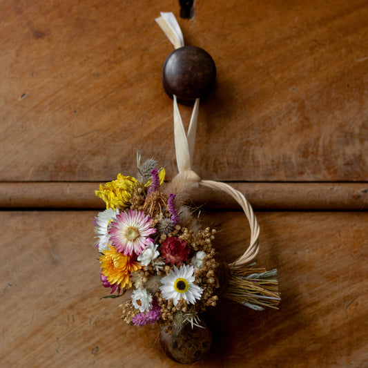 dried flower mini wreath hanging hung on via a cream velvet ribbon on a old chest of a bedroom drawer knob.
Yellow dahlia, pink and white strawflowers