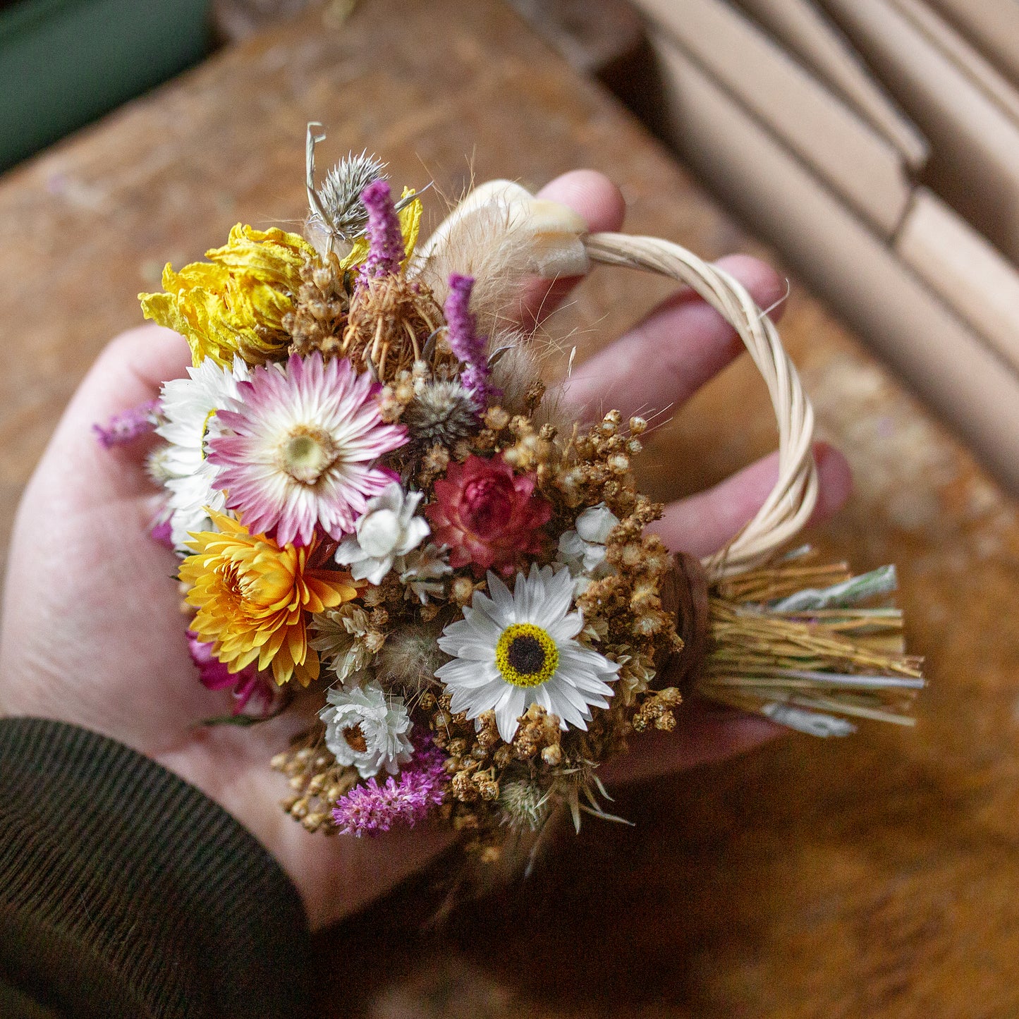 dried flower mini gift size wreath held in a hand over a wooden table