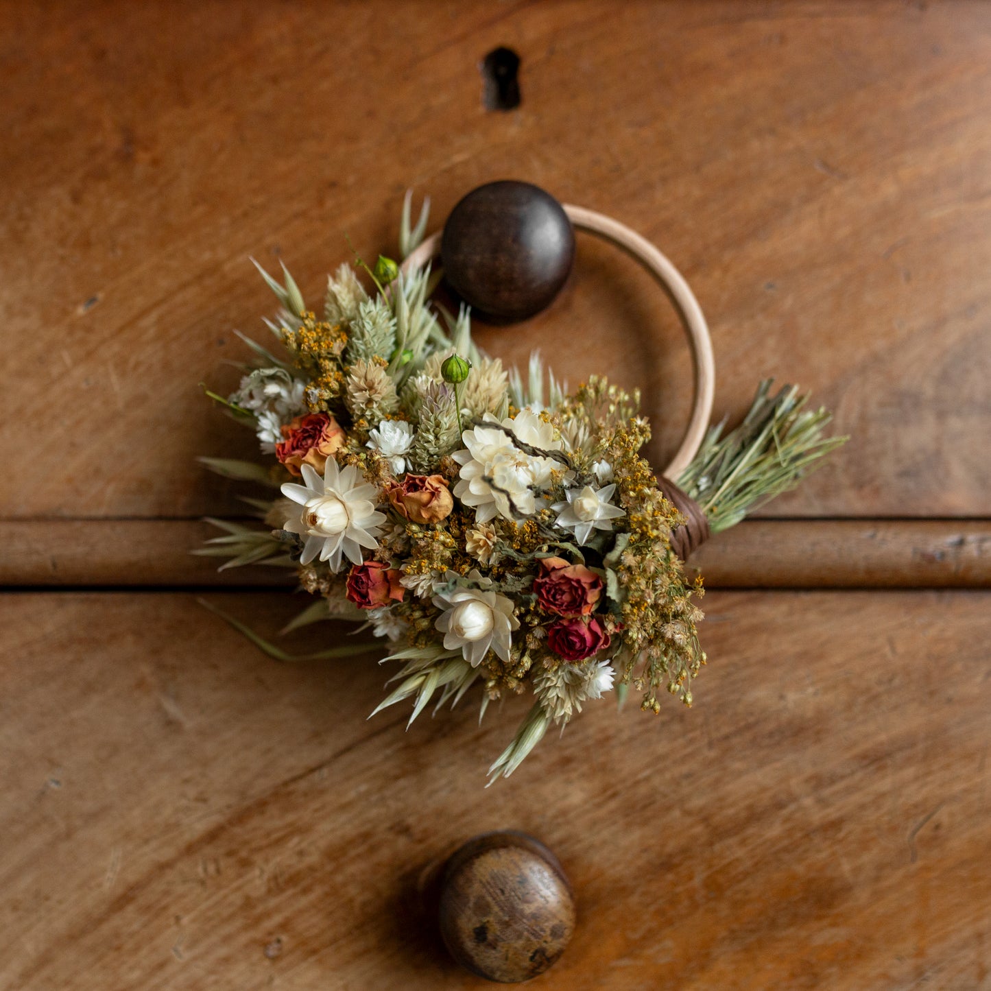 a mini hoop circle wreath made of dried flowers hung on a drawer knob