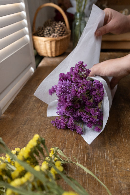 violet dried statice bunch laid on a work surface being wrapped up in paper