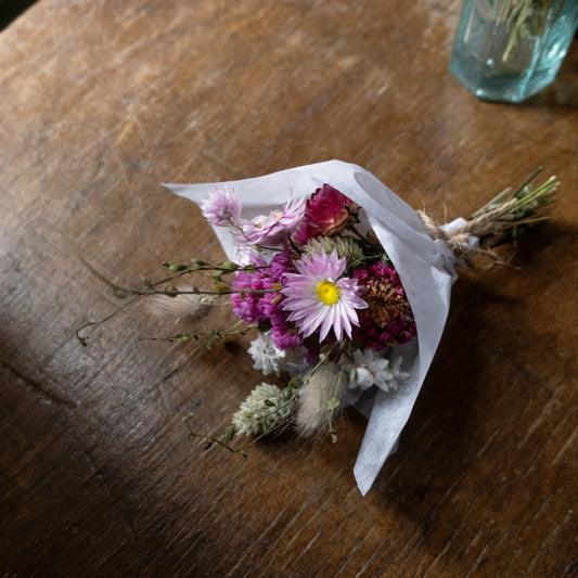 small flower posy wrapped in white tissue paper and tied together with twine. the posy is laying on a wooden table
