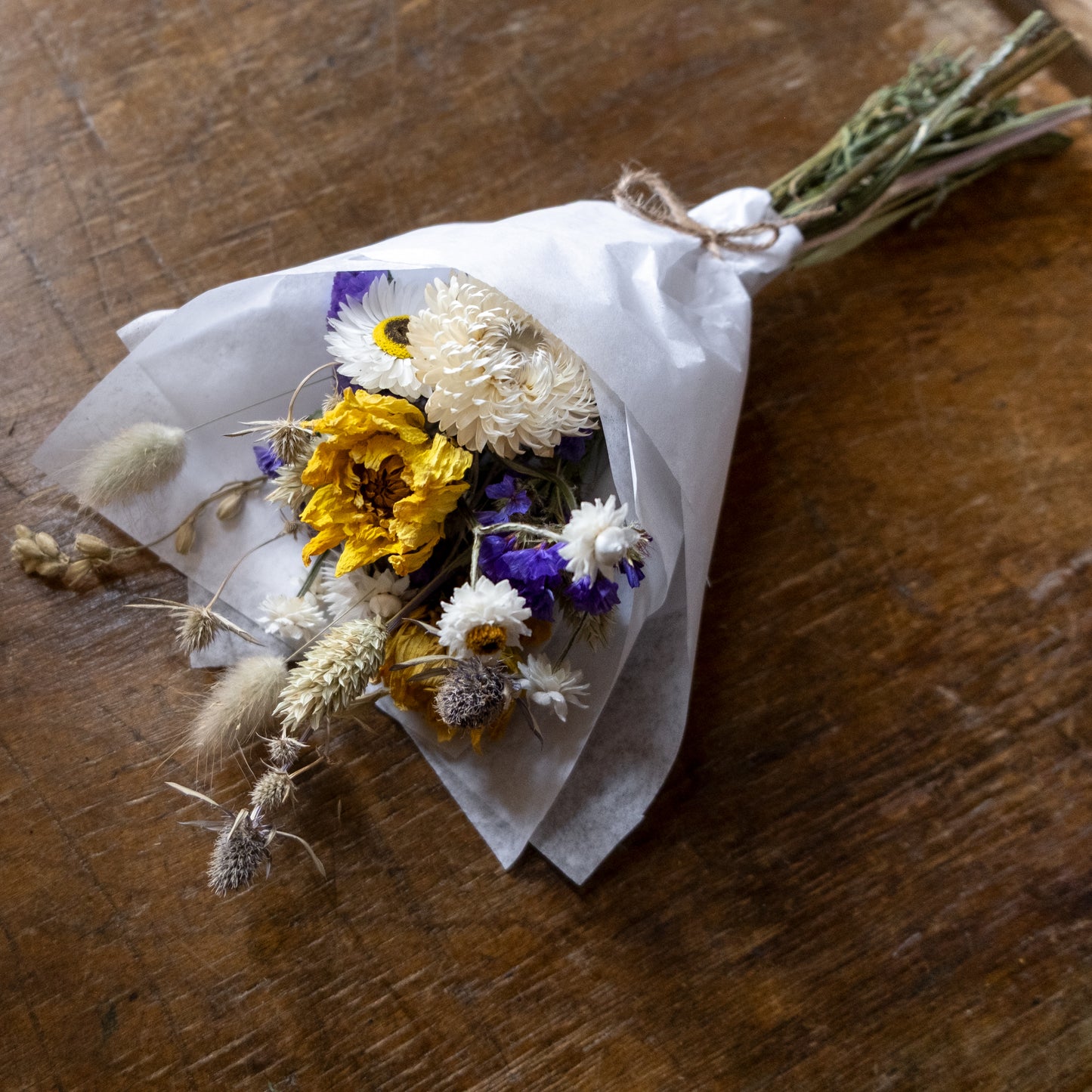 posy small Bouquet of dried flowers wrapped in white tissue paper on a wooden table