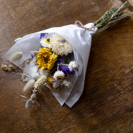 posy small Bouquet of dried flowers wrapped in white tissue paper on a wooden table