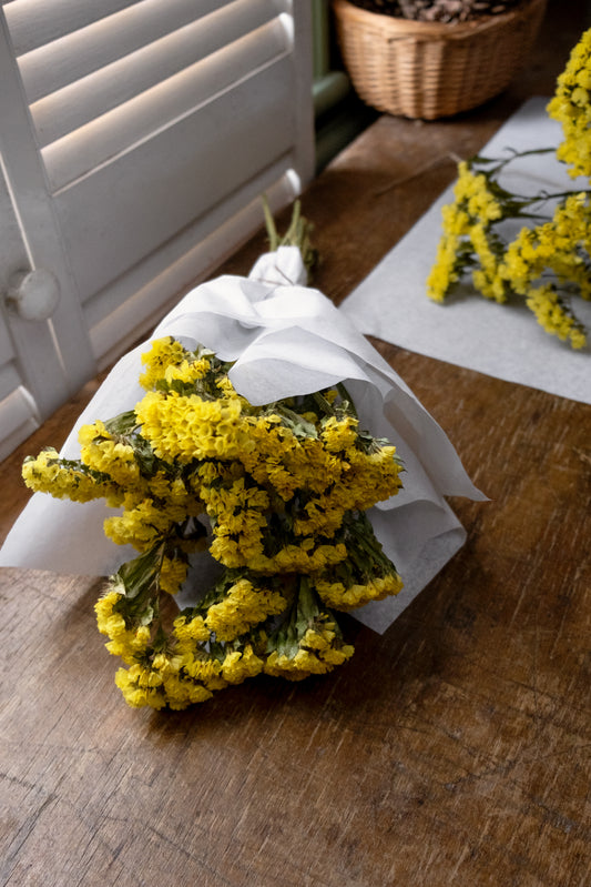 bunch of yellow statice dried flowers wrapped in white tissue paper tied with twine laid on wooden table top